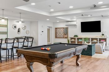 A pool table is in the middle of a room with a tv on the wall.